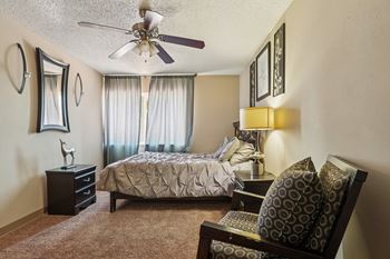 A bedroom with a bed, chair, and a ceiling fan